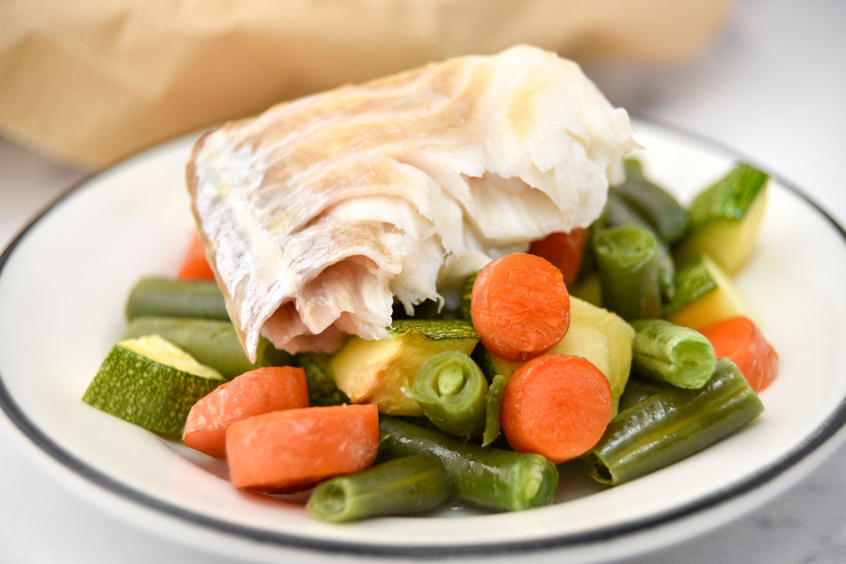 Sheet pan baked cod, green beans, carrots, and zucchini on a plate.
