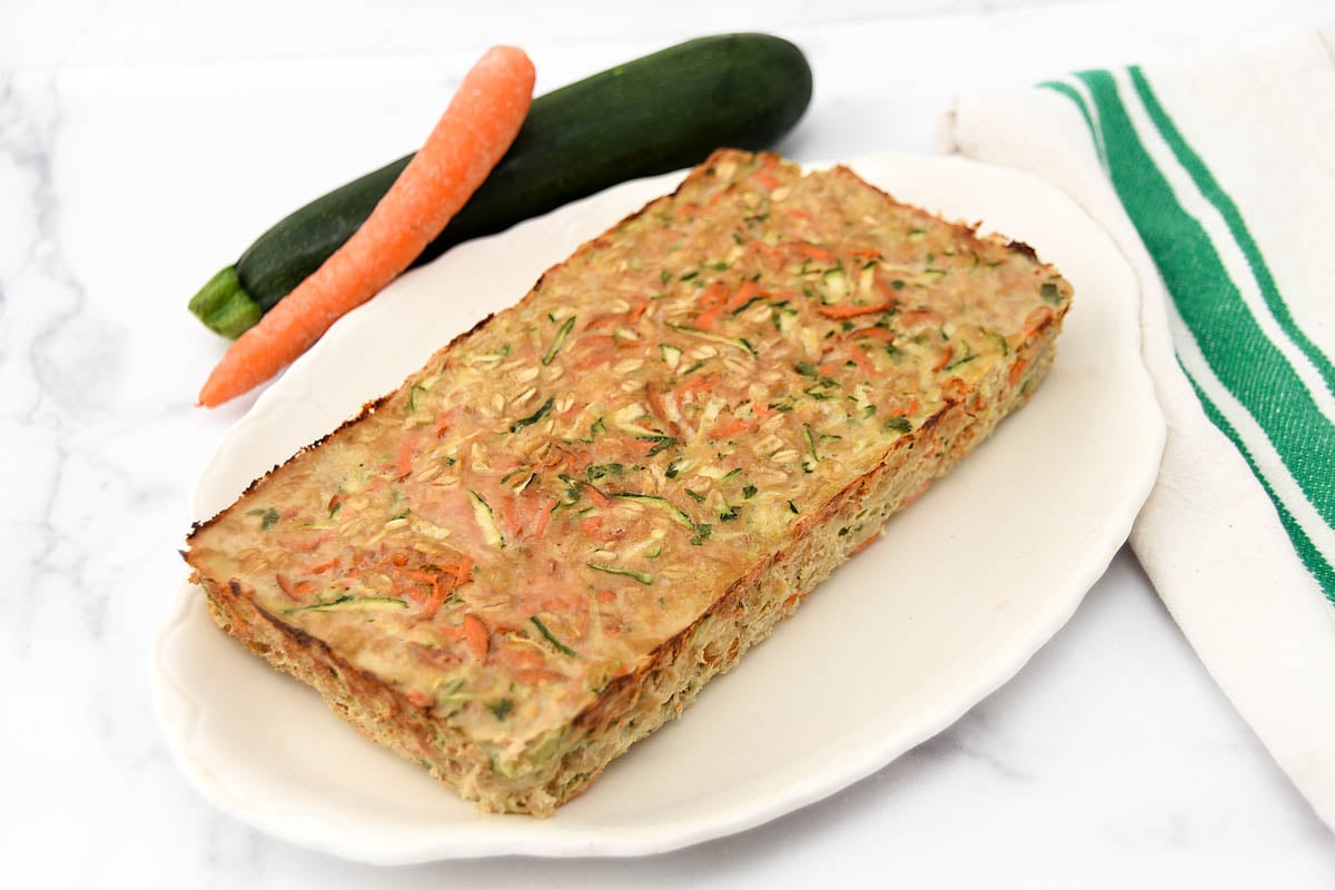 Homemade chicken meatloaf for dogs on a platter, a carrot, and a zucchini.