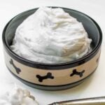 Homemade whipped cream for dogs in a dog bowl and a dollop on a spoon.