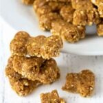 A stack of homemade dog treats made without flour next to a plate of the treats.
