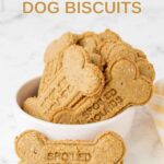 Homemade bone-shaped peanut butter dog biscuits in a bowl and one against it.