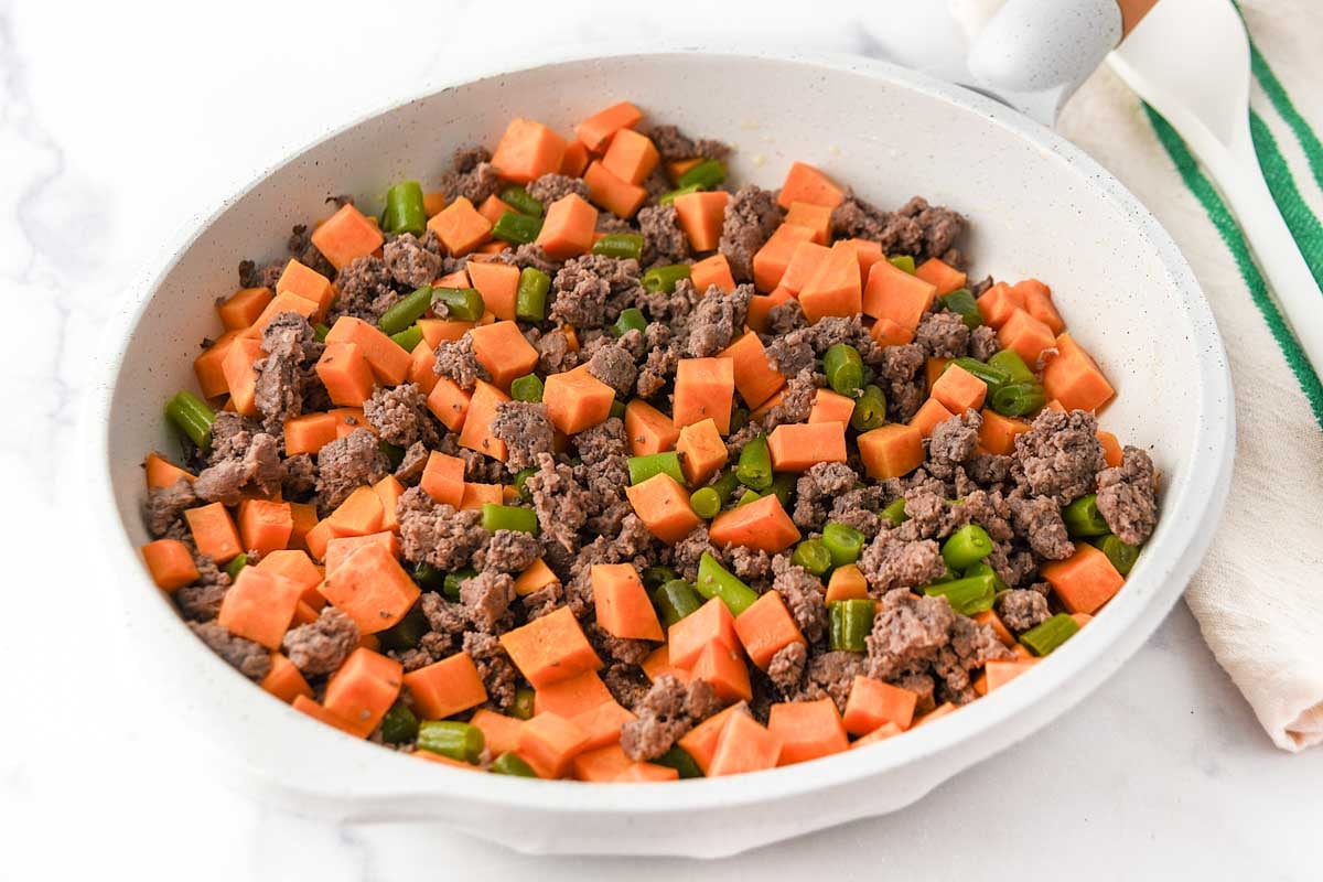 Cooked ground lamb, sweet potato, and green beans in a skillet.