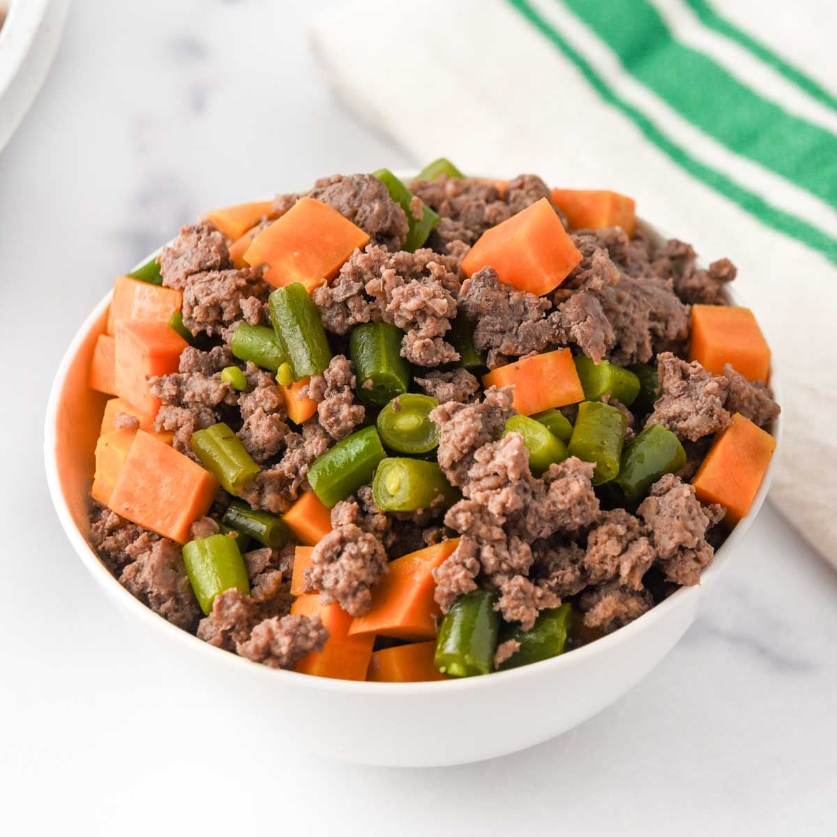 Homemade lamb and sweet potato dog food in a bowl on a marble surface.