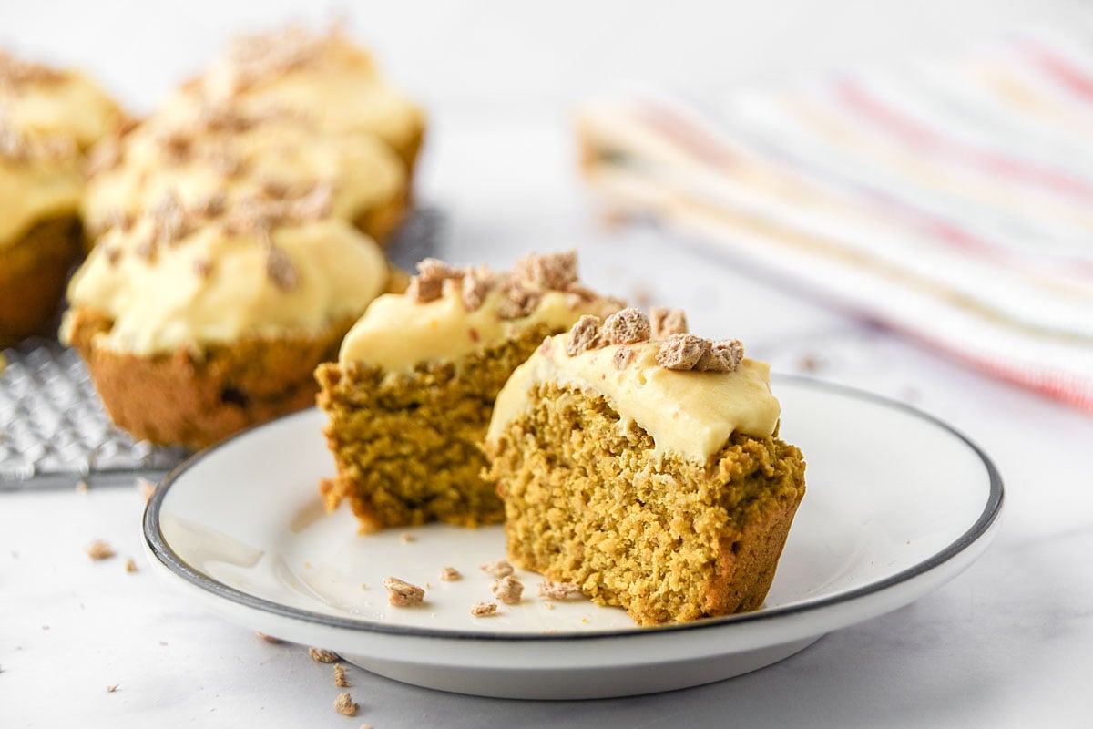 Frosted pumpkin pupcake cut in half on a plate.