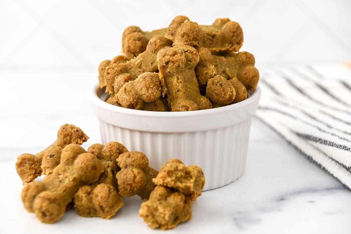 Bone-shaped homemade anchovy dog treats in a small bowl and a few next to it.