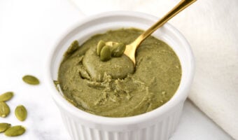 A bowl of homemade pumpkin seed butter with a spoon in it and a few seeds on top.