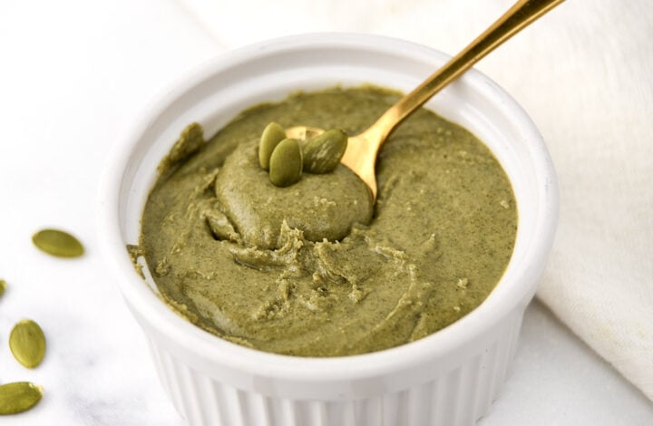 A bowl of homemade pumpkin seed butter with a spoon in it and a few seeds on top.